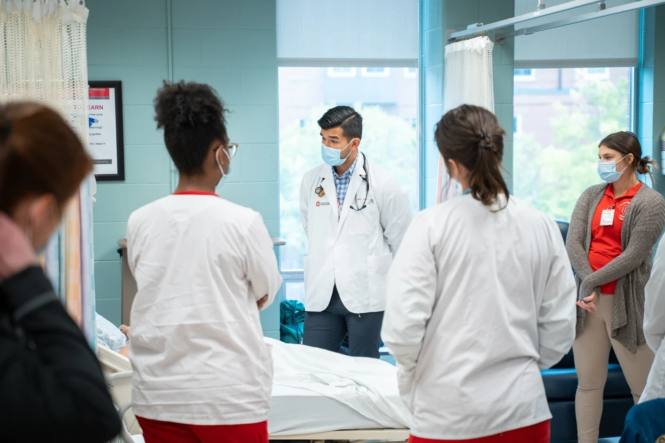 Students standing around a patient while an educator teaches