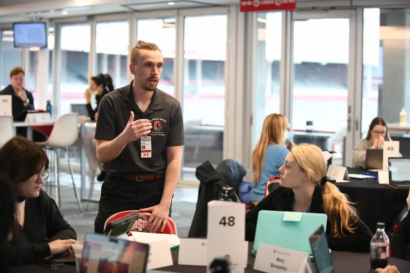 A facilitator speaking to a group of students sitting around a table.