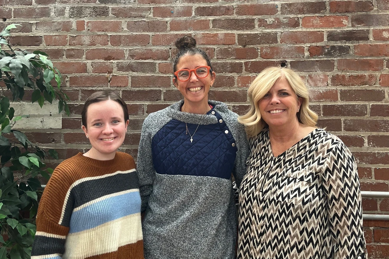 Photo of three women standing in front of a brick wall