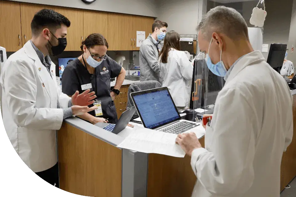 Clinical team working through a patient case standing in a circle with laptops open in front of them