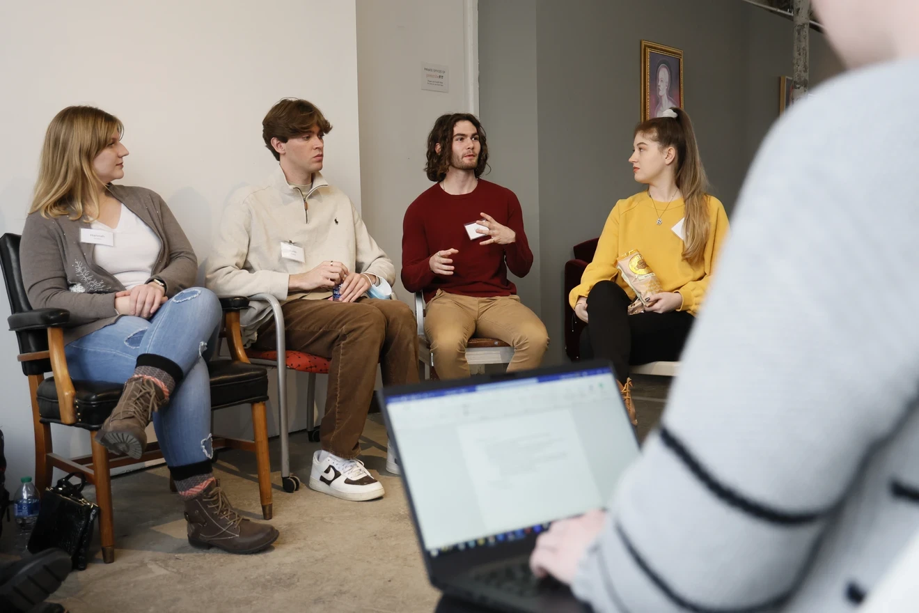 Students sitting in a circle talking while another student takes notes