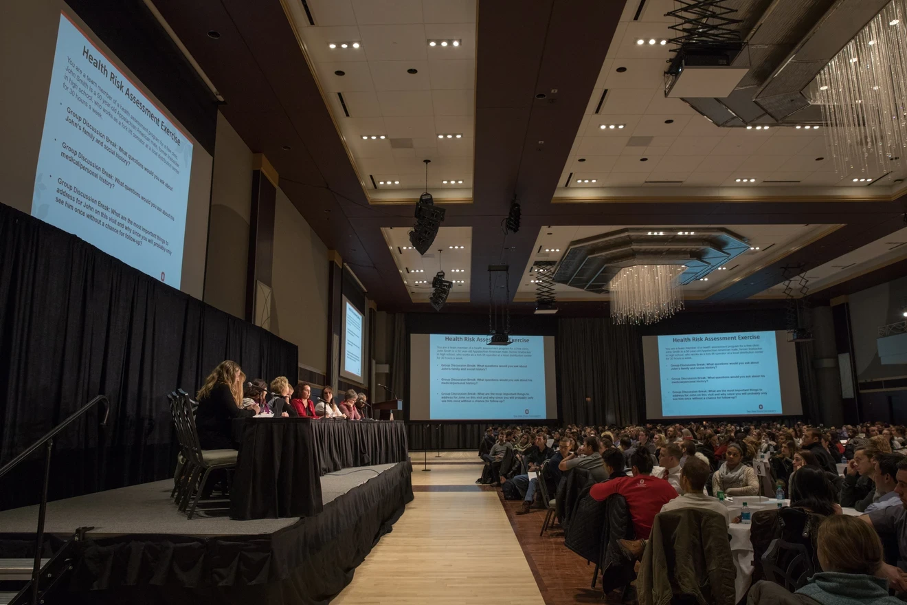 large conference room with screens showing an individual presenting