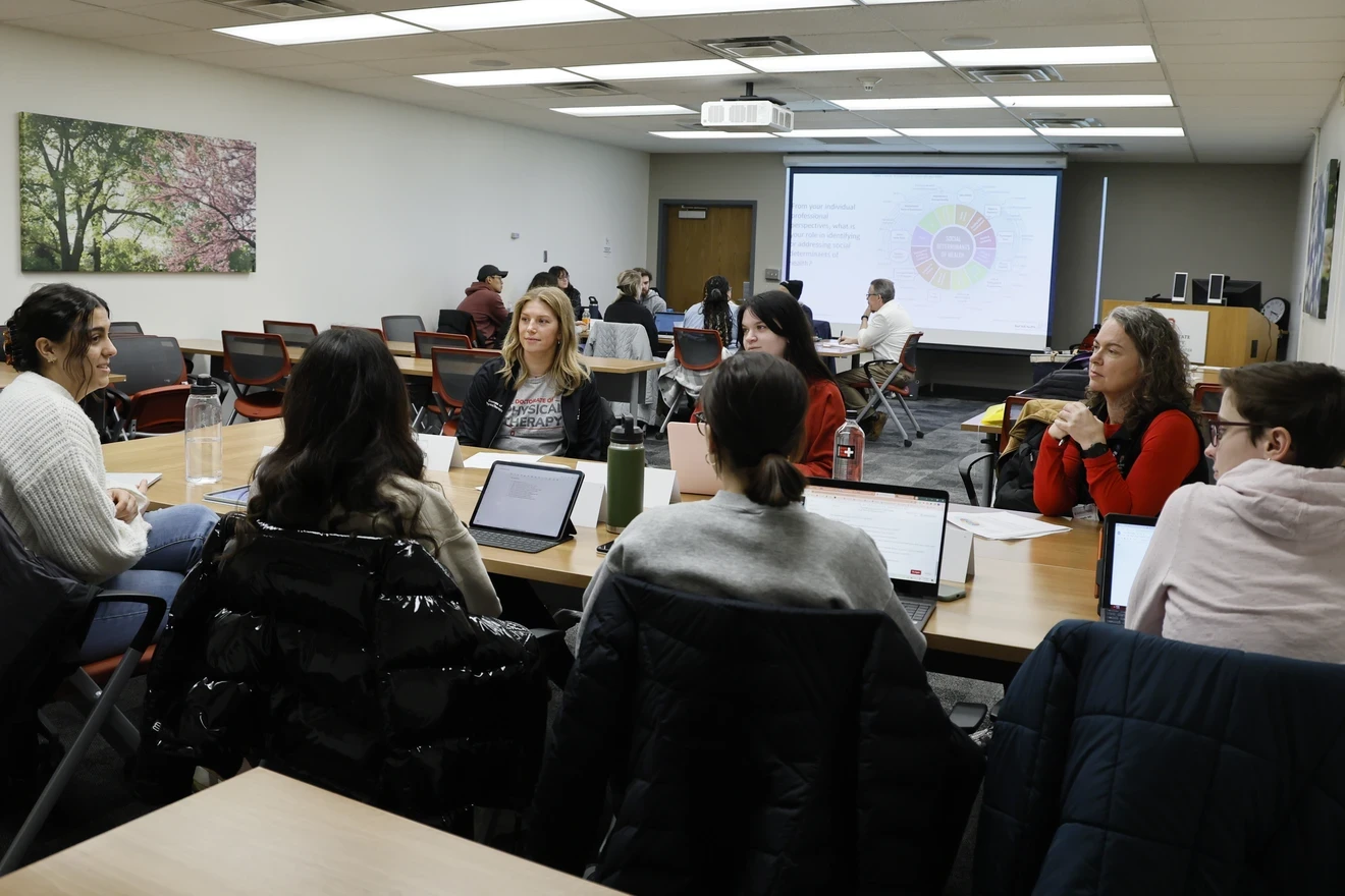 two tables of students, talking together with some laptops open on the desk between them