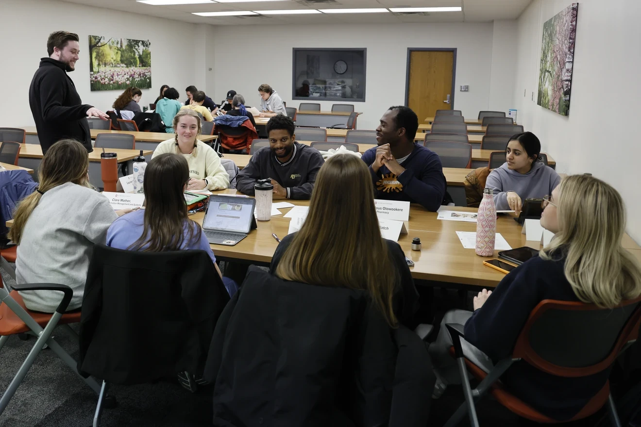 A facilitator talking to students sitting at a table working through puzzles.