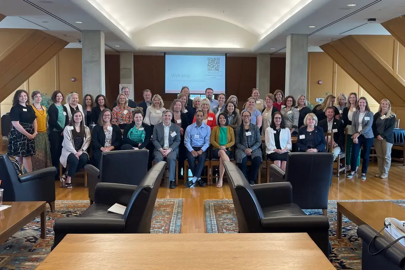 Photo group shot of the attendees of the meeting, sitting in chairs and standing in front of a room