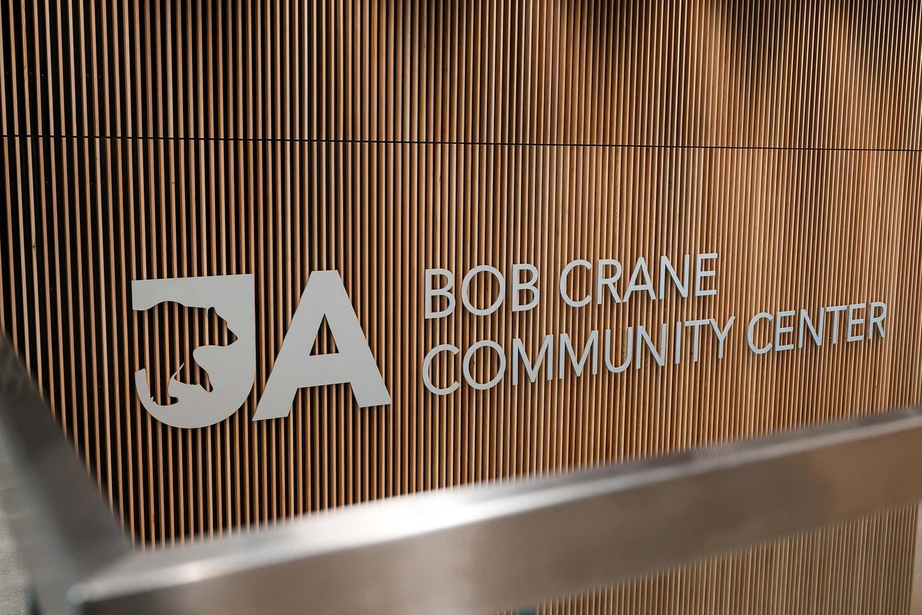 A photograph of the logo of the Bob Crane Community Center. The logo is printed in silver on a wood background